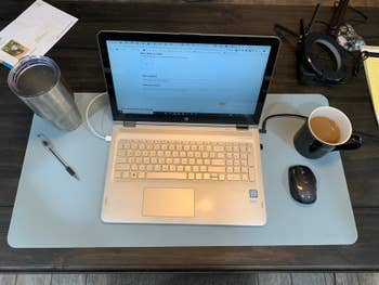 a reviewer image of the blue desk mat with laptop, coffee, mouse and pen on it 