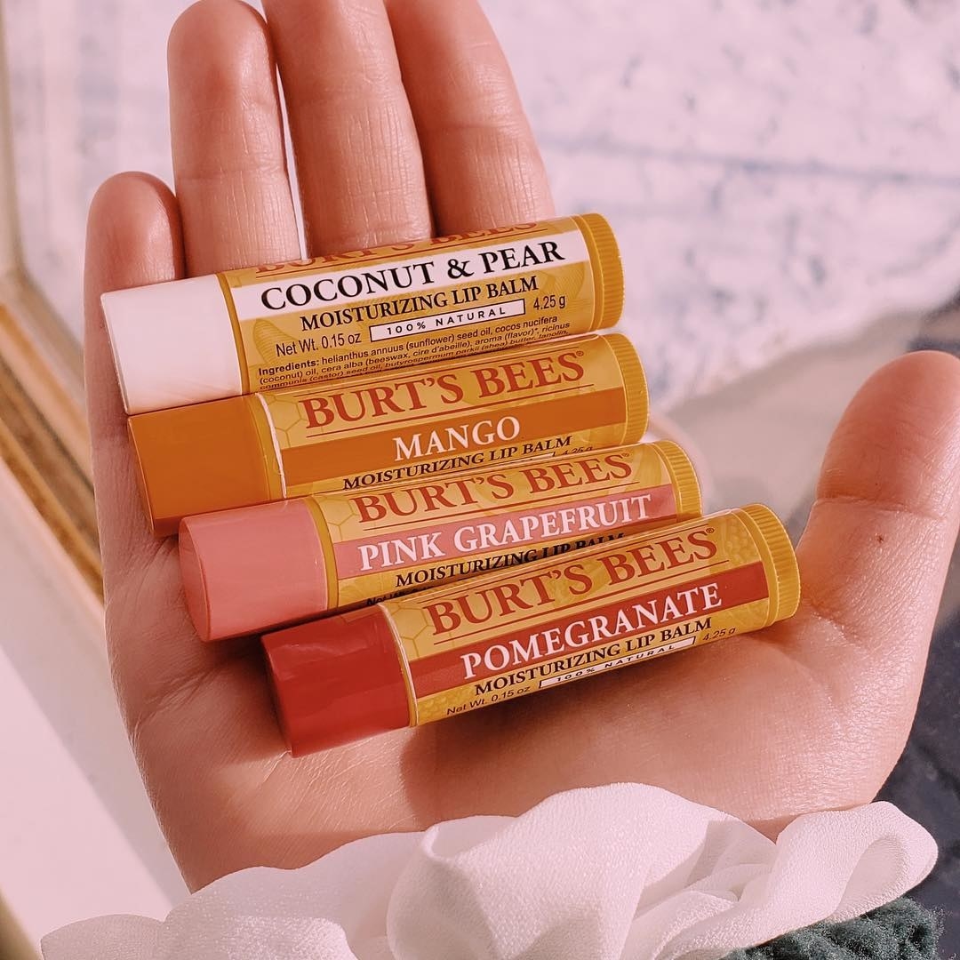 A person&#x27;s hand holding four tubes of lip balm