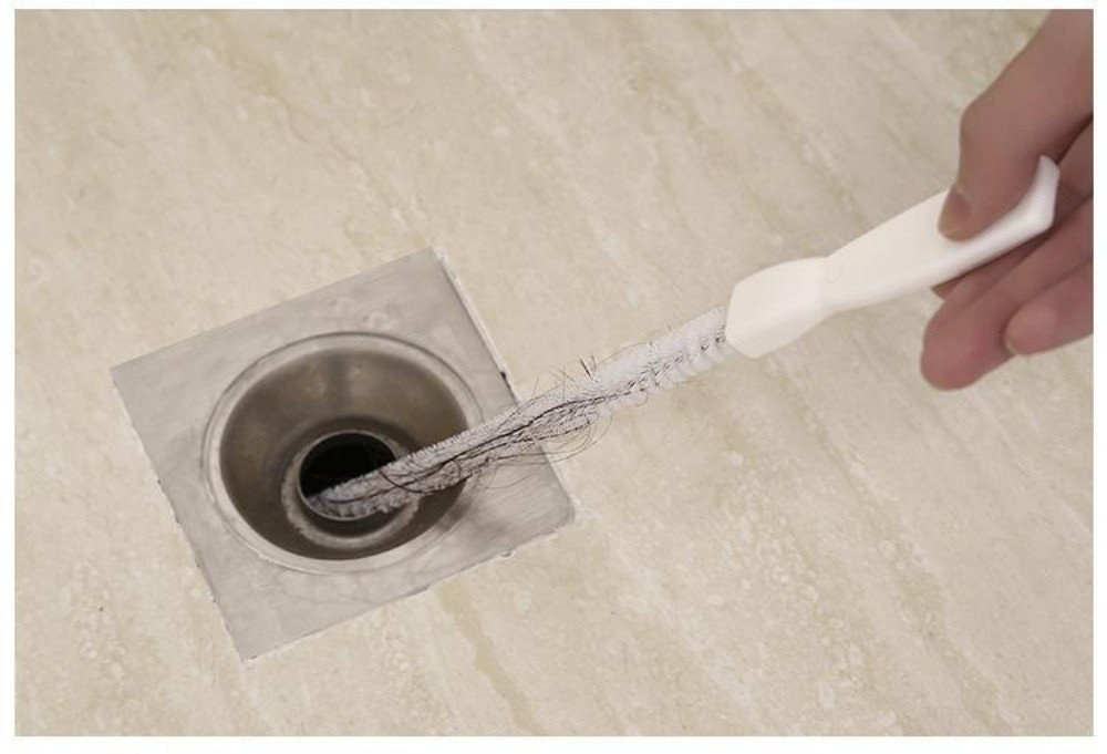 A person using a drain snake on a bathroom drain to clear hair out of it