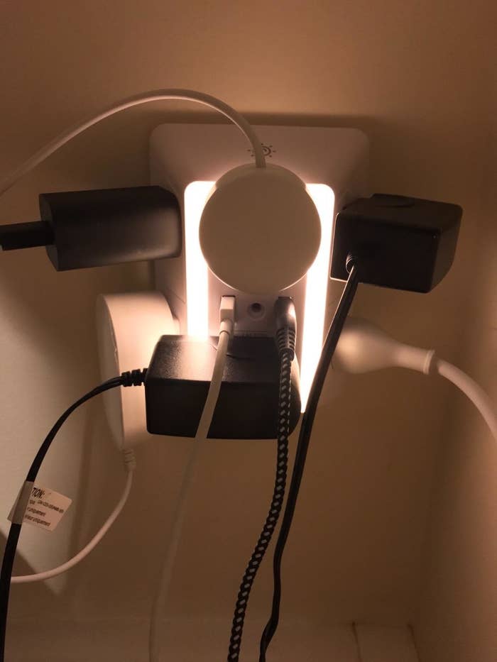 A wall outlet charger with a nightlight and several large chargers attached to it plus two USB cords 