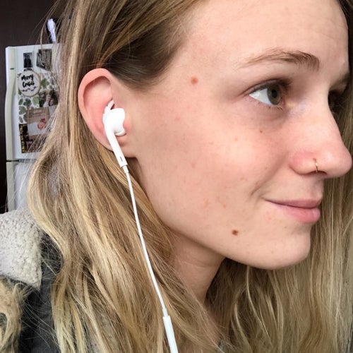 A reviewer wearing Apple Ear Buds with the hooks installed to keep them secure
