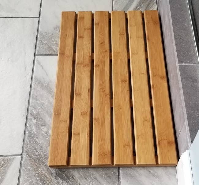 a reviewer's slatted light brown bamboo mat on the floor of their bathroom 