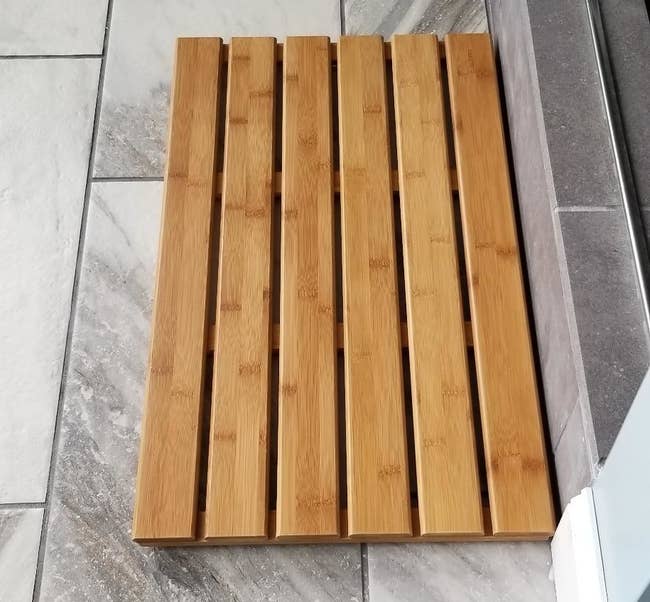 a reviewer photo of the slatted natural bamboo mat on the floor of their bathroom 