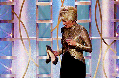 an awards show host holding a cocktail and a pair of heels that she then tosses over her shoulder. The heels get tossed, not the cocktails. We don&#x27;t toss cocktails.