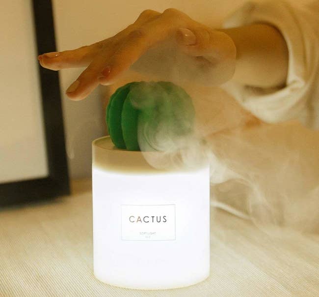 A small, lit-up white humidifier with a teensy green cactus emerging from it 