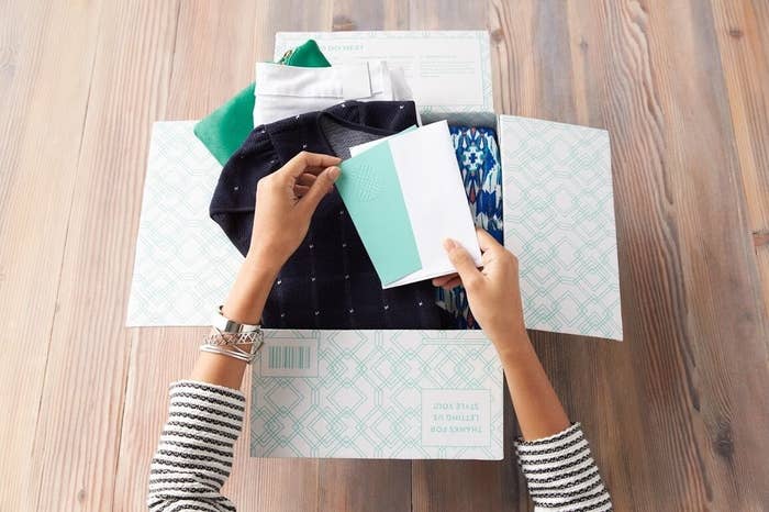 Hand opens styling card in Stitch Fix subscription box filled with clothes