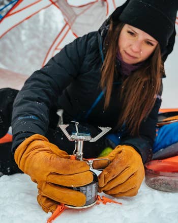 model putting small propane tank under stove stand while camping in snow