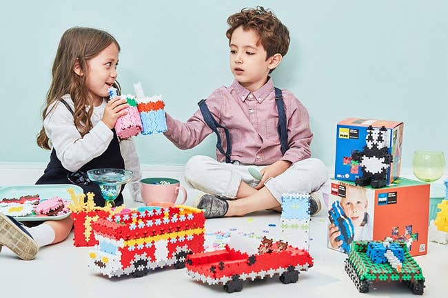 Two child models playing with vehicles and animals created with colorful puzzle blocks