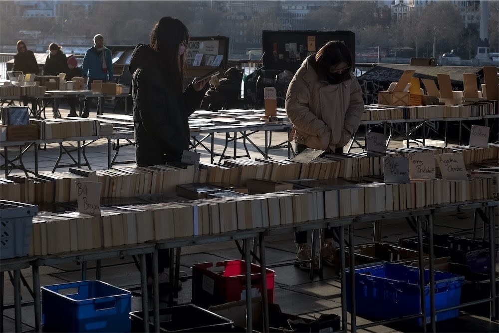 Two women wear face masks as they look at books on the South Bank