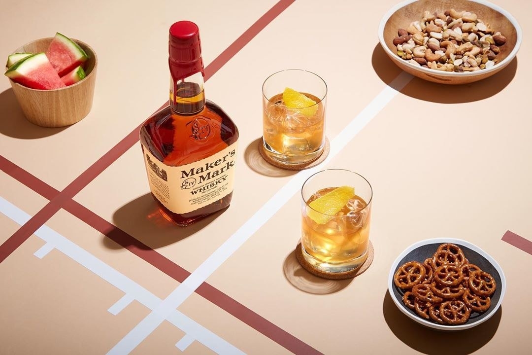 maker&#x27;s mark bottle, two cocktails, and three bowls of snacks