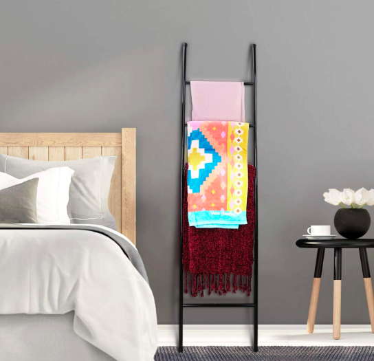Display ladder with folded blankets and scarves next to a bed