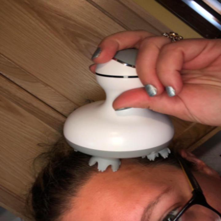 reviewer pic of person using the handheld massager on scalp near forehead