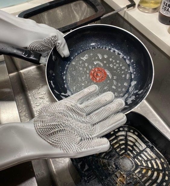 Hands using the scrubbing gloves to wash a pan
