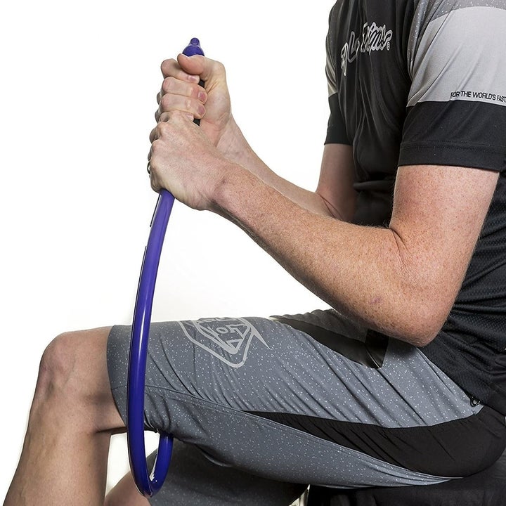 person sitting and using the tool to massage the back of thigh