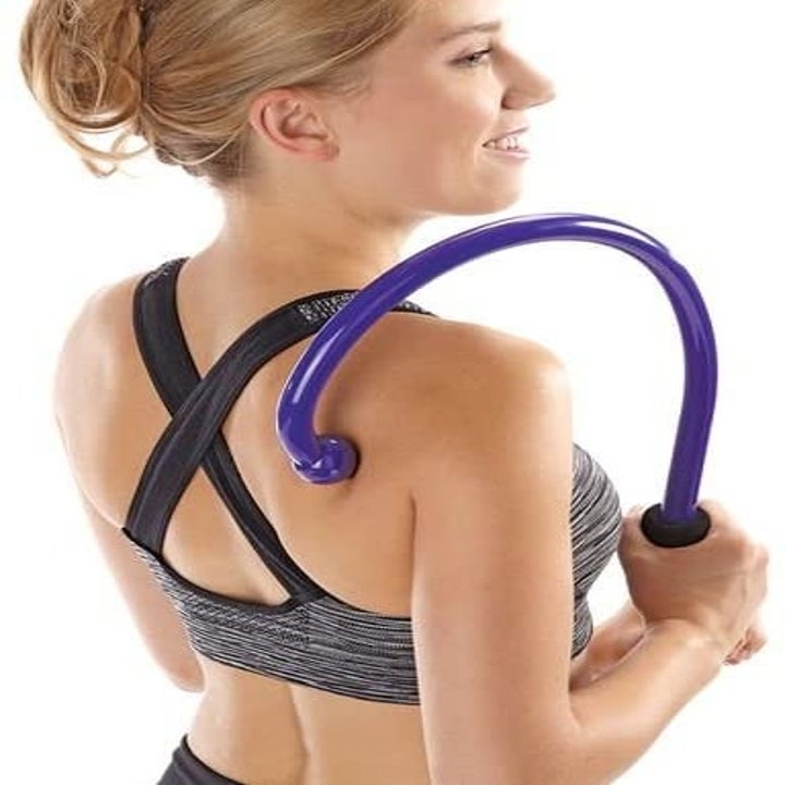 person standing and using the tool to massage their upper back