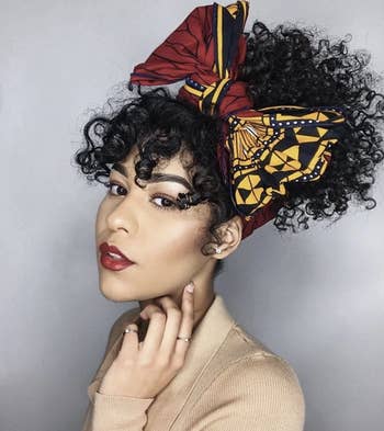 Model wearing a maroon and yellow printed head wrap tied in a bow