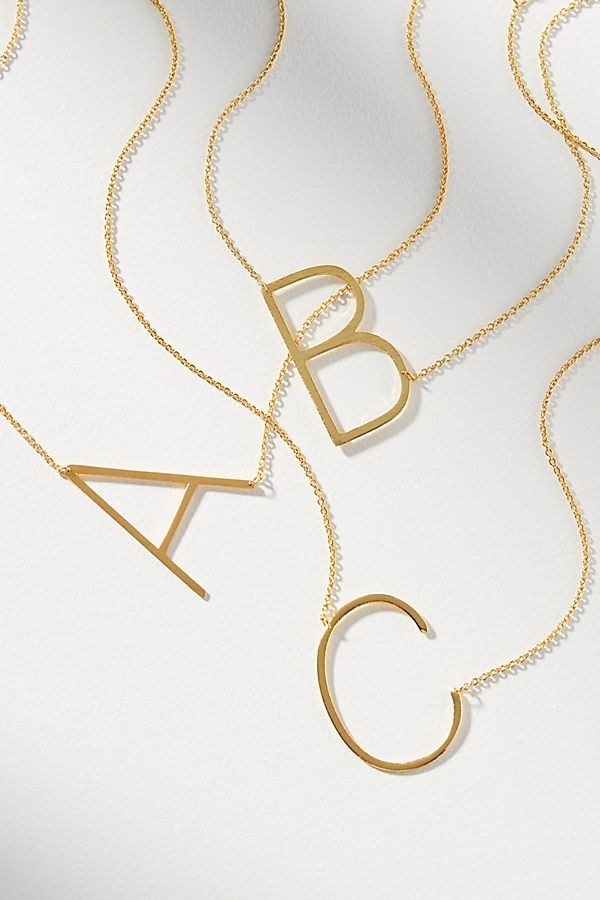 three gold necklaces with oversized initials on them