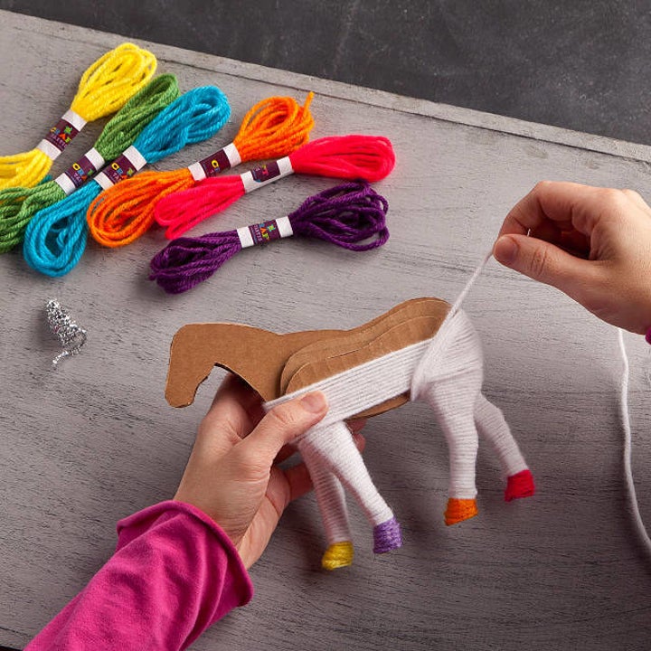 A person covering the cardboard horse cutout in yarn