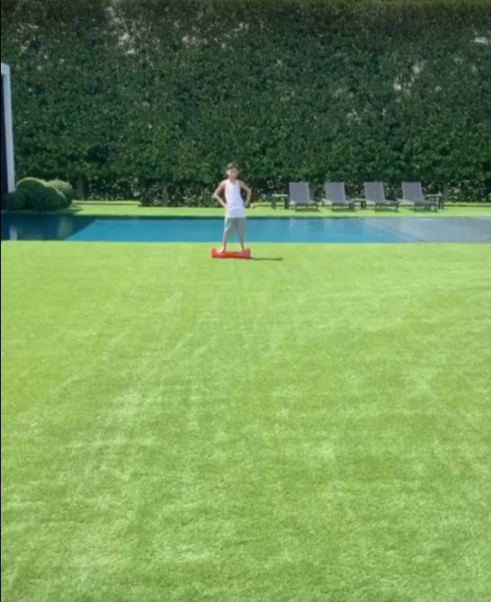 J Lo's son standing on a hoverboard in front of their swimming pool in her large manicured backyard