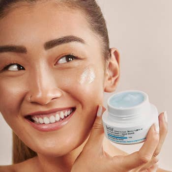 A person holding the product jar with the cream on their face