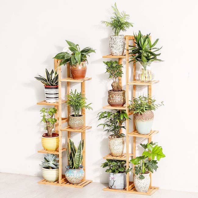 A five tier and six tier plant stand made of light wood with potted plants resting on them 