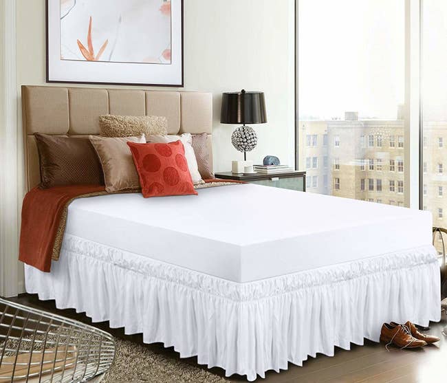 A bed with white sheets and a white dust ruffle all along its edges 