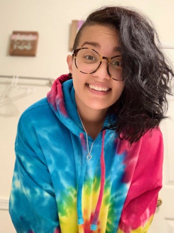 A person wearing a bright tie-dye hoodie with drawstrings on the hood