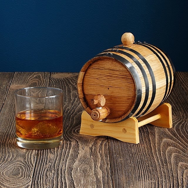A small whiskey barrel next to a glass of whiskey 