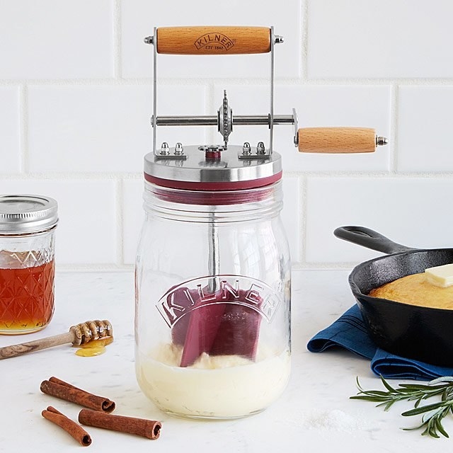 A glass mini butter churner with a lid and a handle for churning the inside spatula 