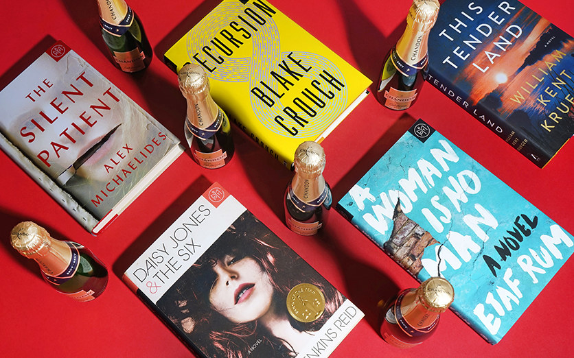 five books lying on a table next to bottles of champagne