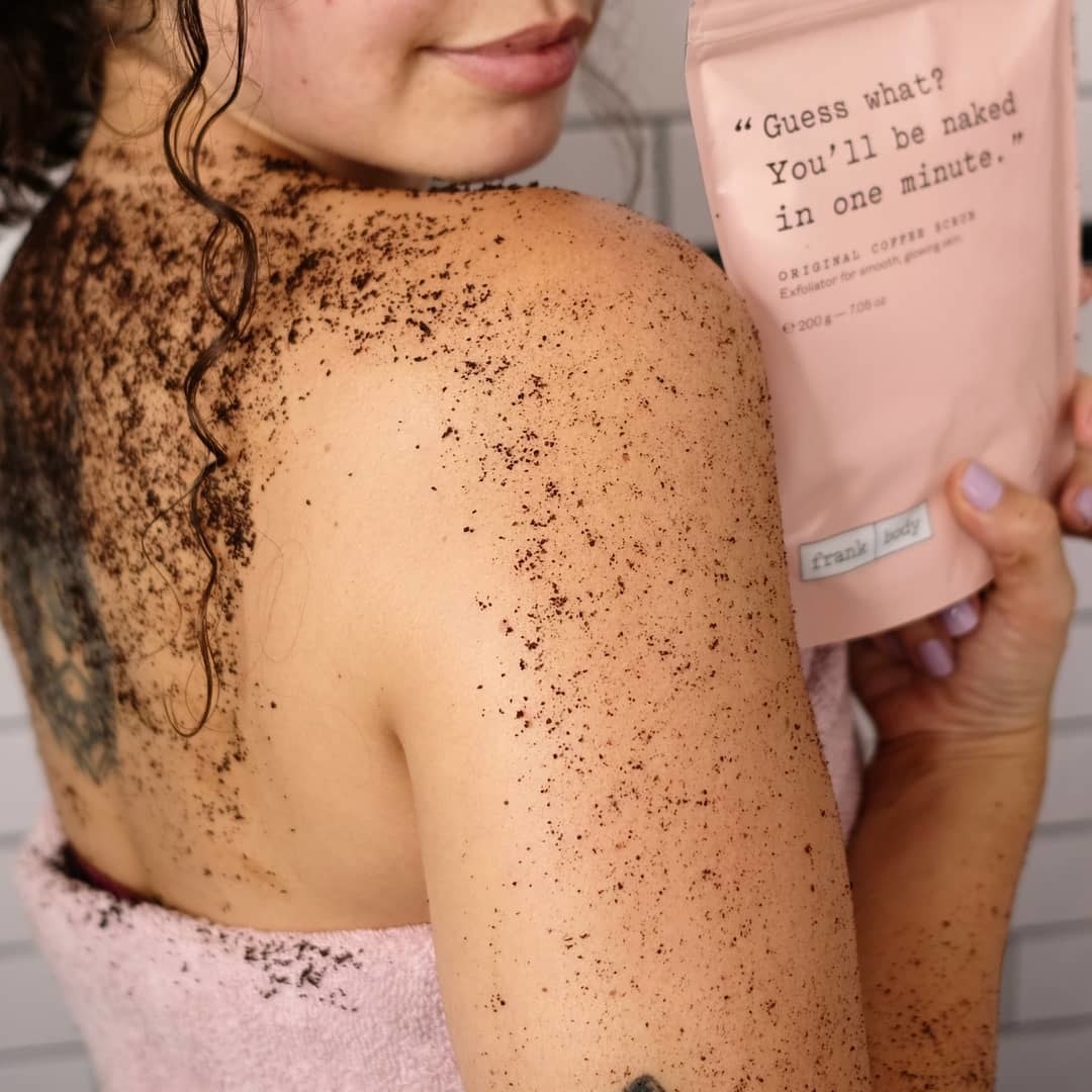 model with the coffee scrub on her back, shoulder, and arm, holding the bag of product