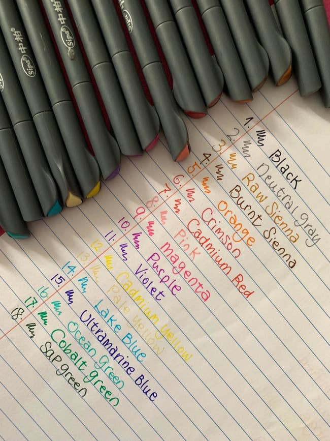 18 pens in different colors next to writing showing their color and fine point thin-ness 