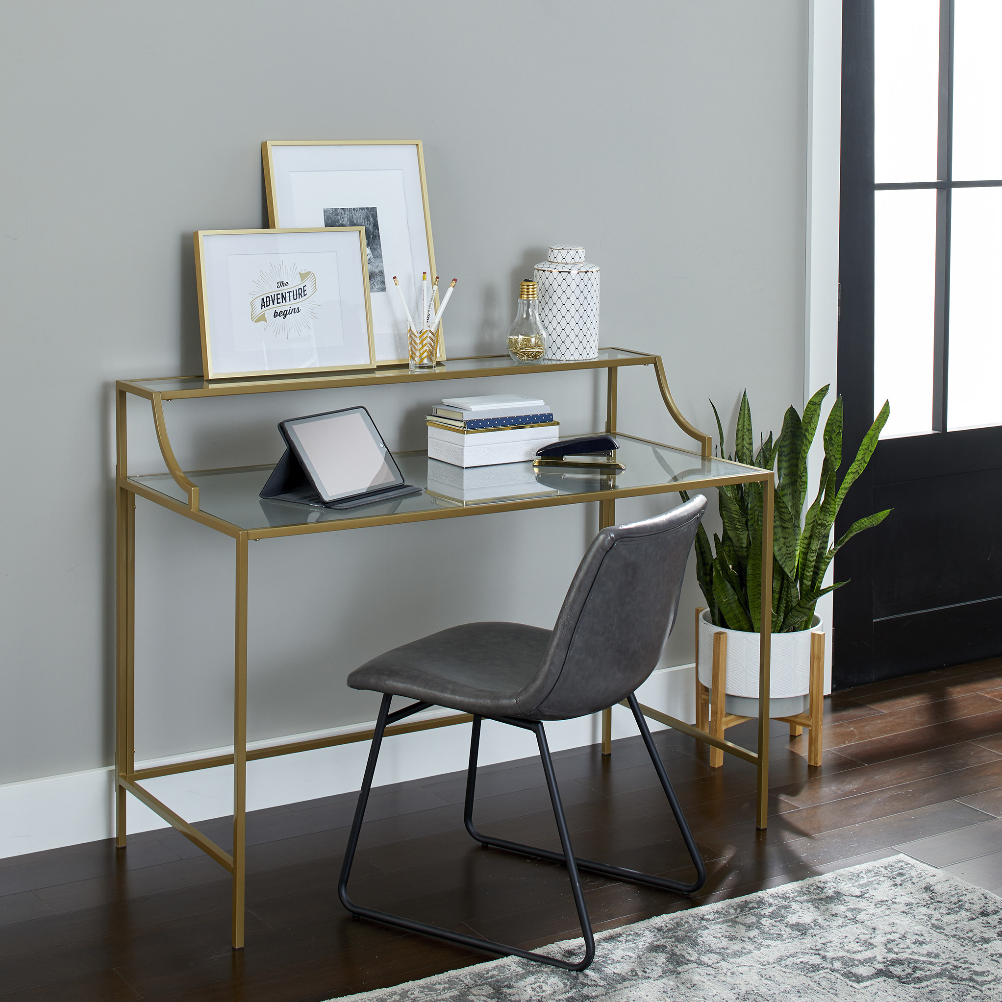 the glass desk with gold detailing,  a gray chair, and an ipad and other accessories on it