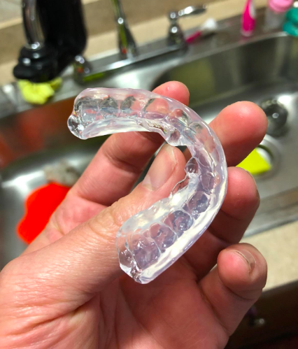 A reviewer&#x27;s hand holding the transparent guard molded to the shape of their teeth
