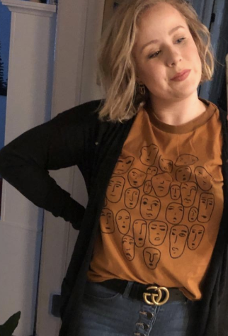 Reviewer wears dark yellow graphic tee with line drawings of stylized faces on the front under a black cardigan