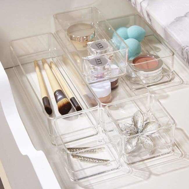 Clear plastic organizers with makeup and jewelry in them in a drawer 