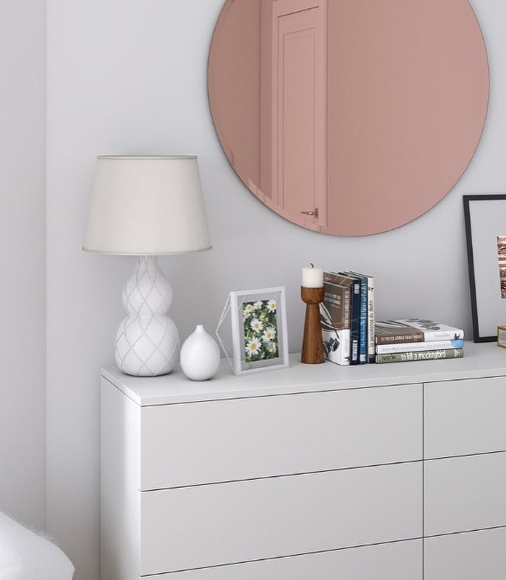 The mirror hanging on a wall above a dresser with décor on it