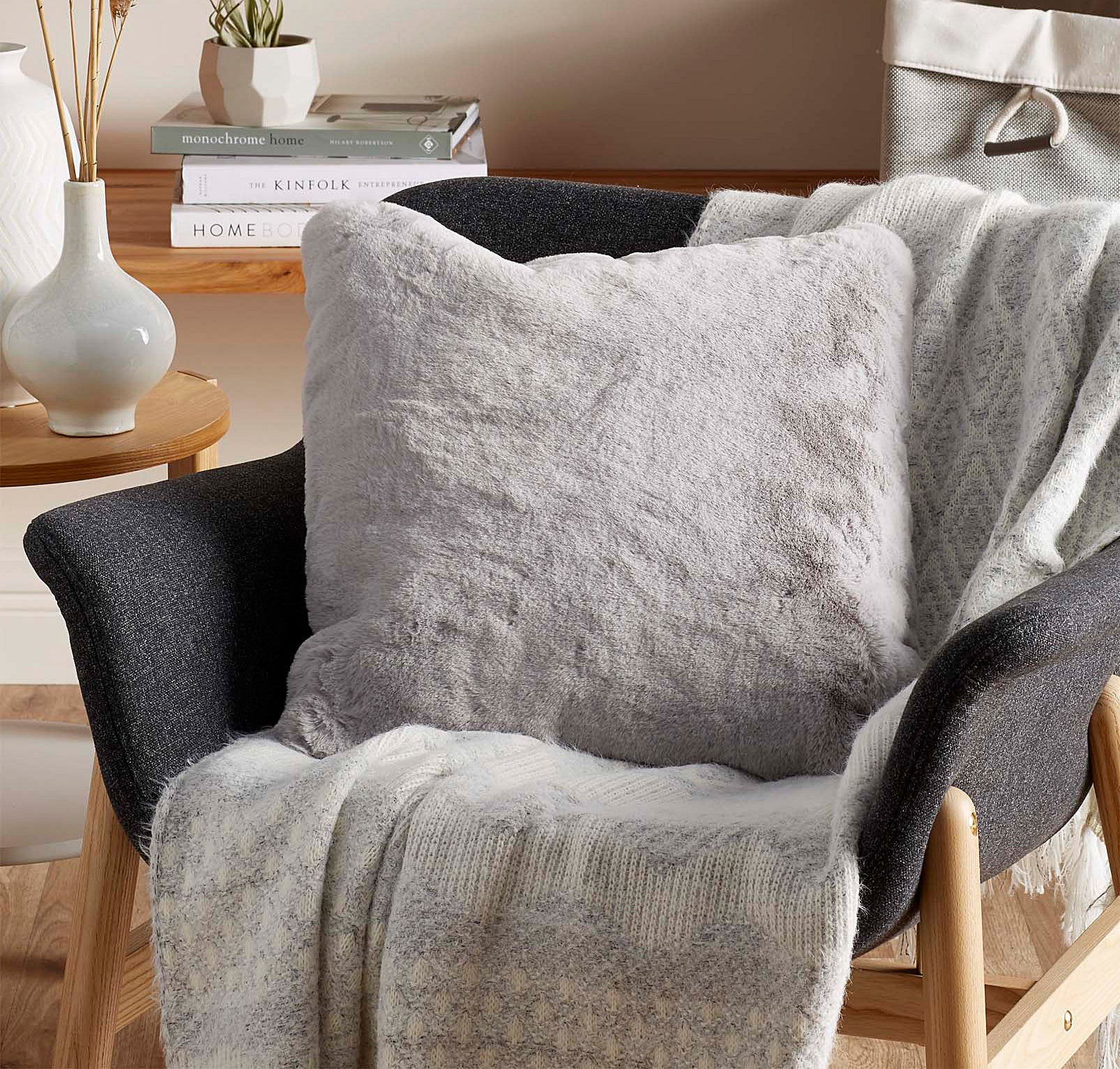 A fluffy throw pillow on a small chair with a blanket