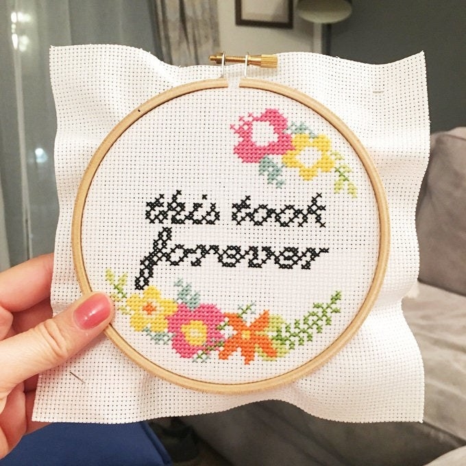 A person holding up a finished floral cross-stitch that says &quot;this took forever&quot; 