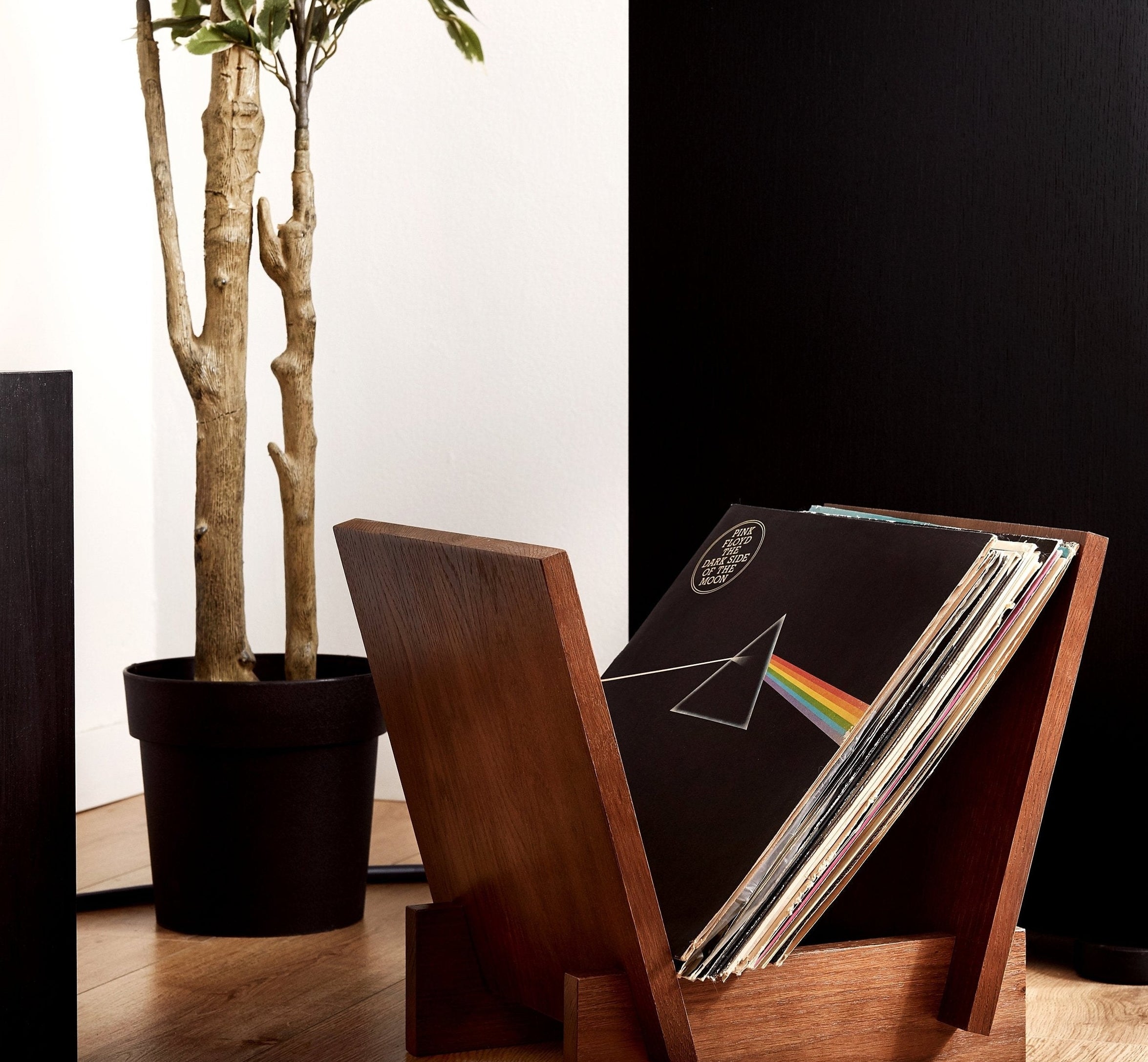 a minimalist dark wood vinyl holder with a flat bottom and V-angled sides holding a stack of records with dark side of the moon on top