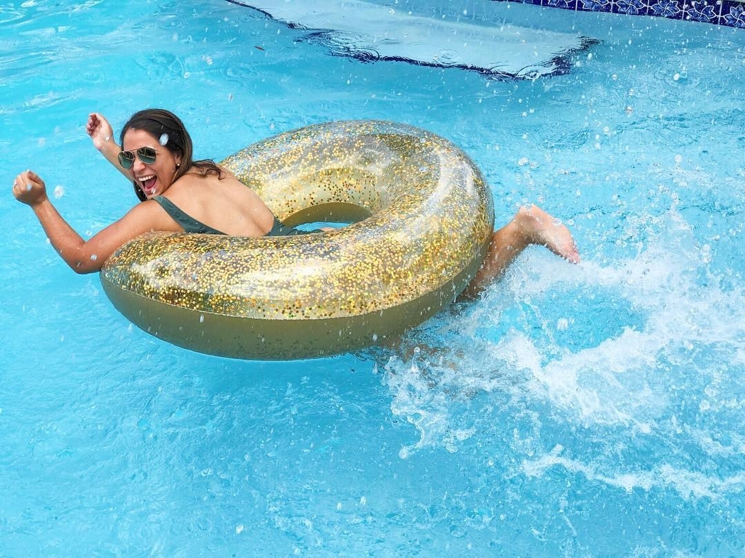 a person laying on their stomach laughing while inside the middle of a glitter filled golden inner tube in a pool