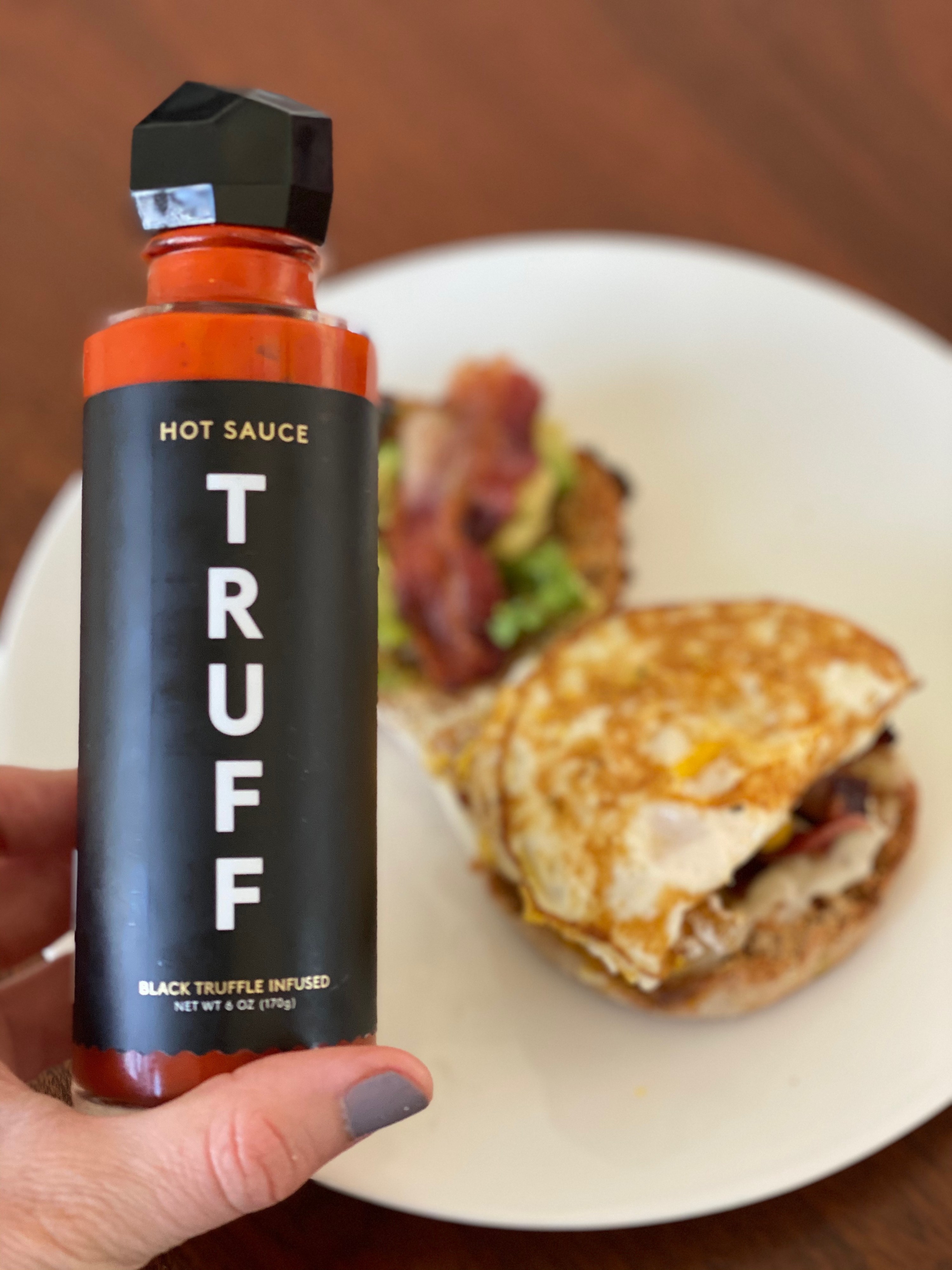 BuzzFeed writer holding a bottle of Truff hot sauce in front of a breakfast sandwich 