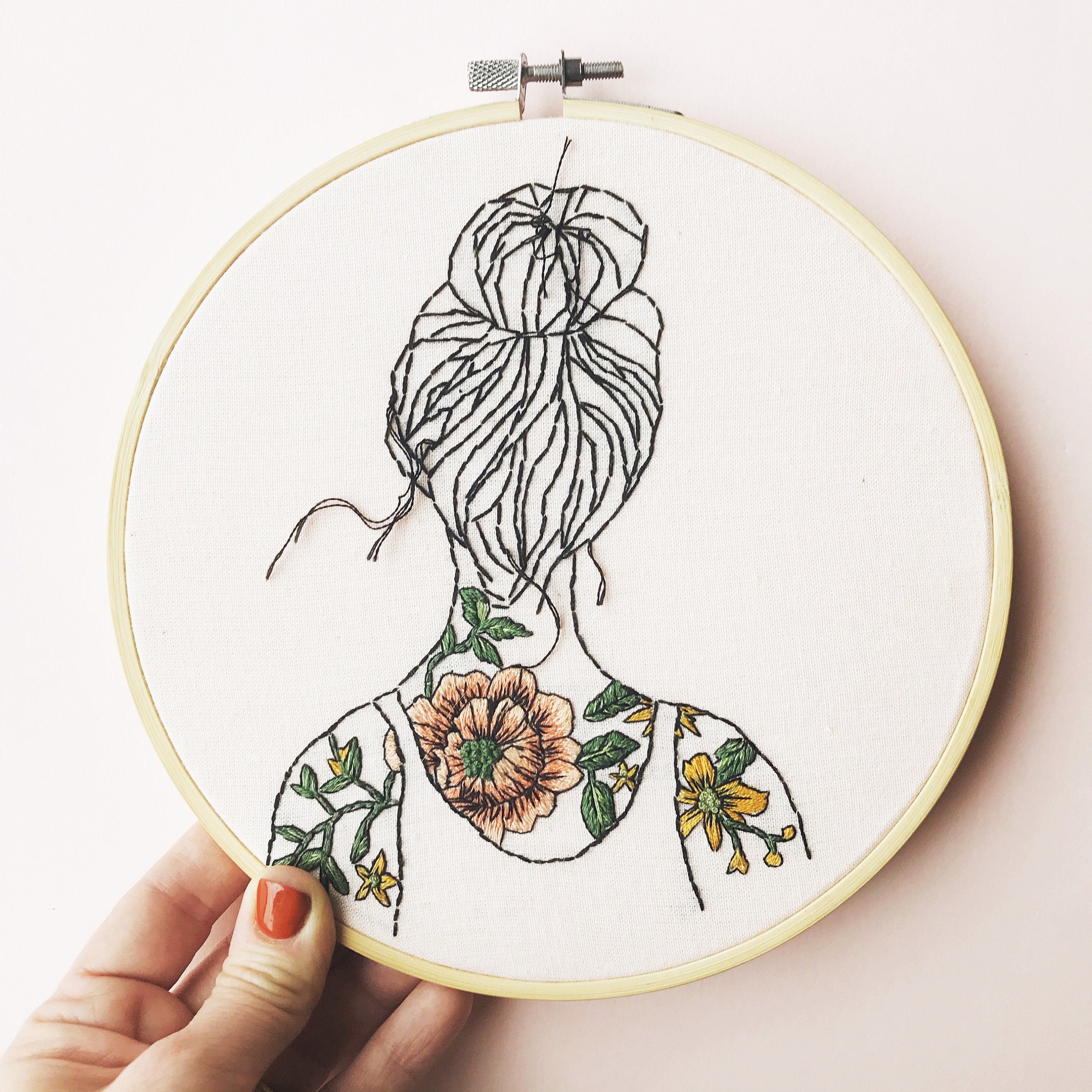 A piece of embroidery inside of a hoop with a sewn image of a person&#x27;s back, covered in floral tattoos 