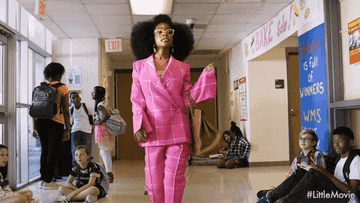 A girl confidently strutting down the school hall in a bright pink suit
