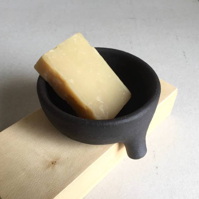 The crockery  holding a barroom  of soap and placed with the spout implicit    the borderline   of a surface