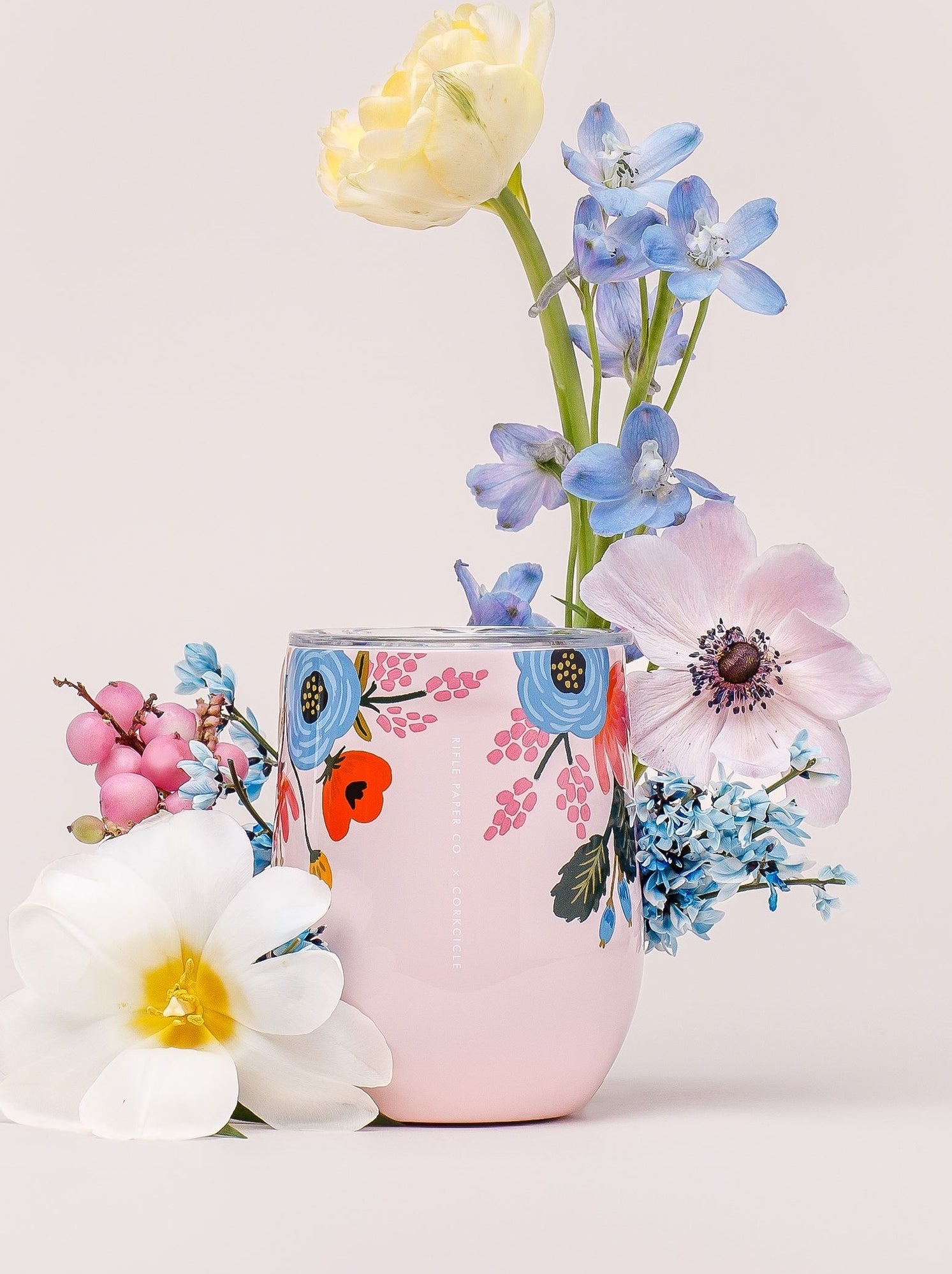 pink steamless wine glass with illustration of blue, red, and pink florals on it and a clear lid