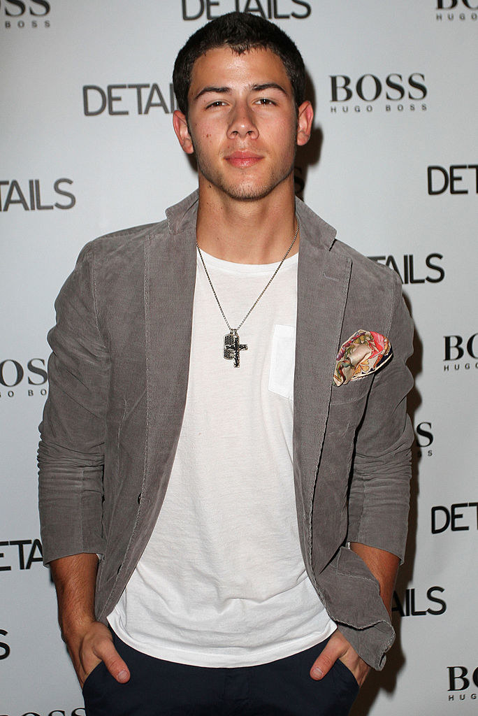 Nick with his hands in his pocket, wearing a white shirt and a cross necklace