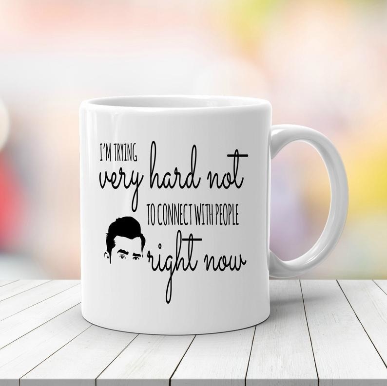 The white mug with David&#x27;s face and black text that reads &quot;I&#x27;m trying very hard not to connect with people right now&quot;