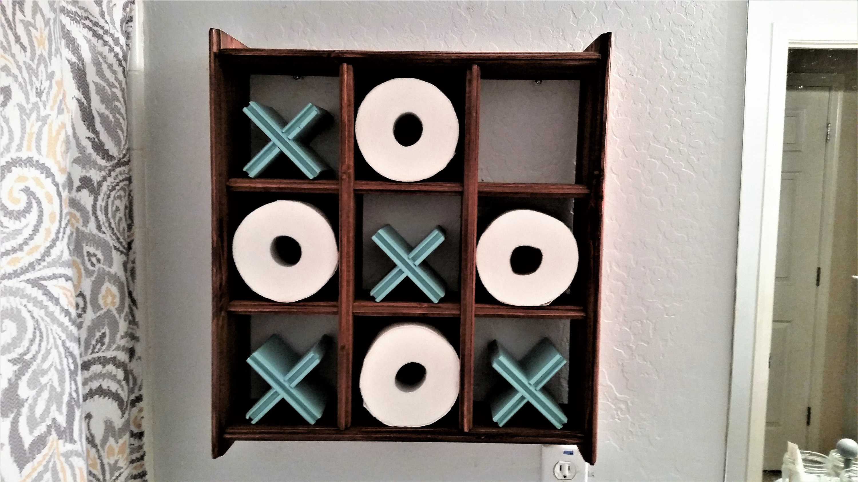 aa shelf with nine squares built in, four of them filled with blue X&#x27;s four others filled with toilet paper as O&#x27;s