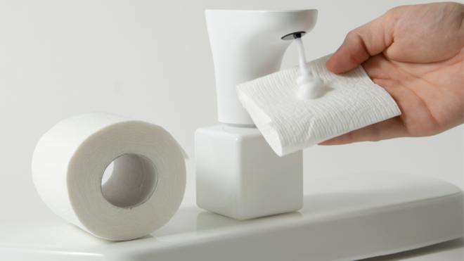 a model holding a piece of toilet paper under the fohm dispenser as it expels foam